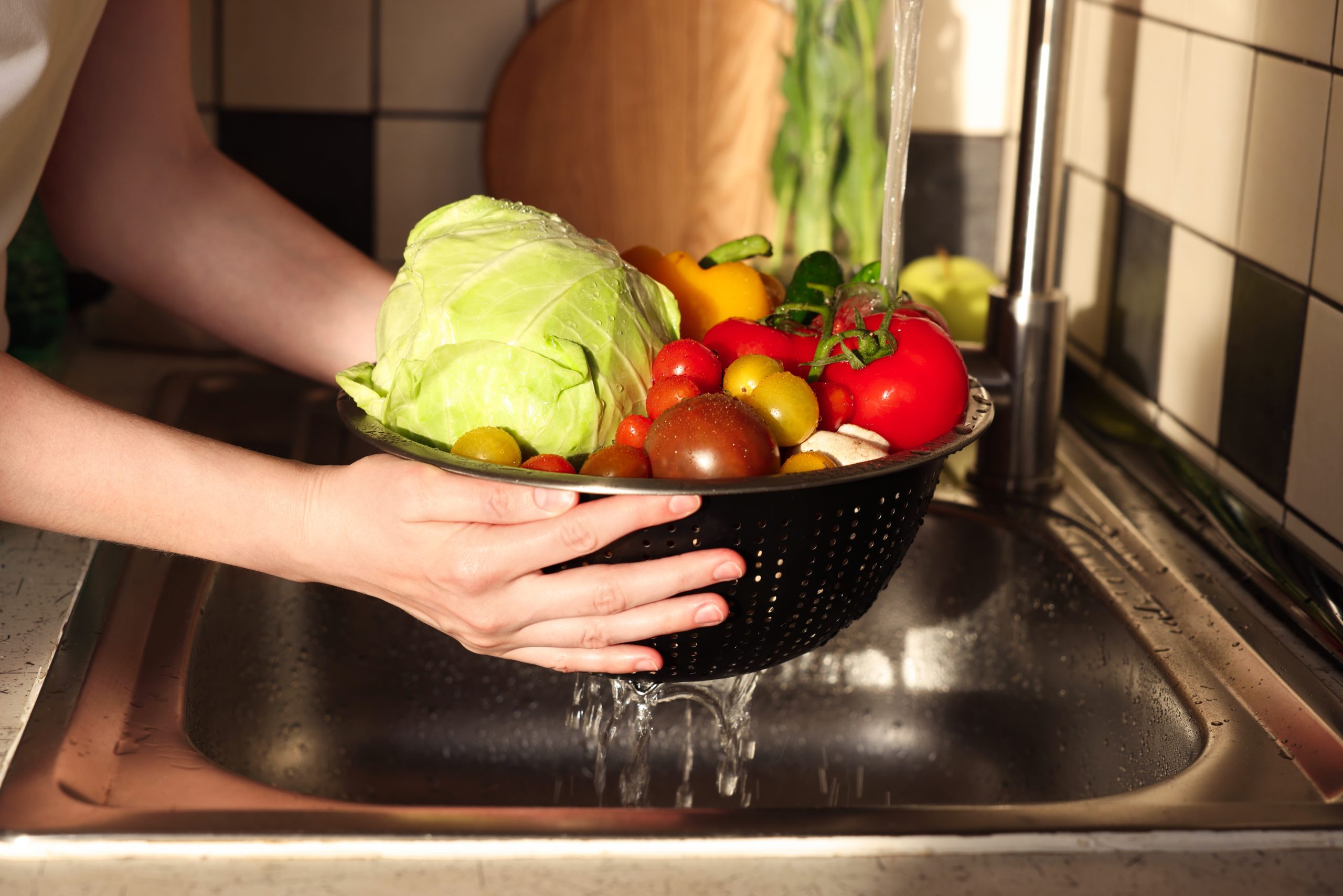 Woman,washing,different,vegetables,in,metal,colander,,closeup